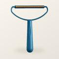 Teal fabric scraper with a brass blade, on a warm cream background