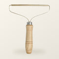 Fur lifter with a turned wood handle and a slim brass blade on a wire frame, on a warm cream background