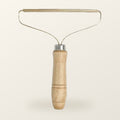 Fur lifter with a turned wood handle and a slim brass blade on a wire frame, on a warm cream background