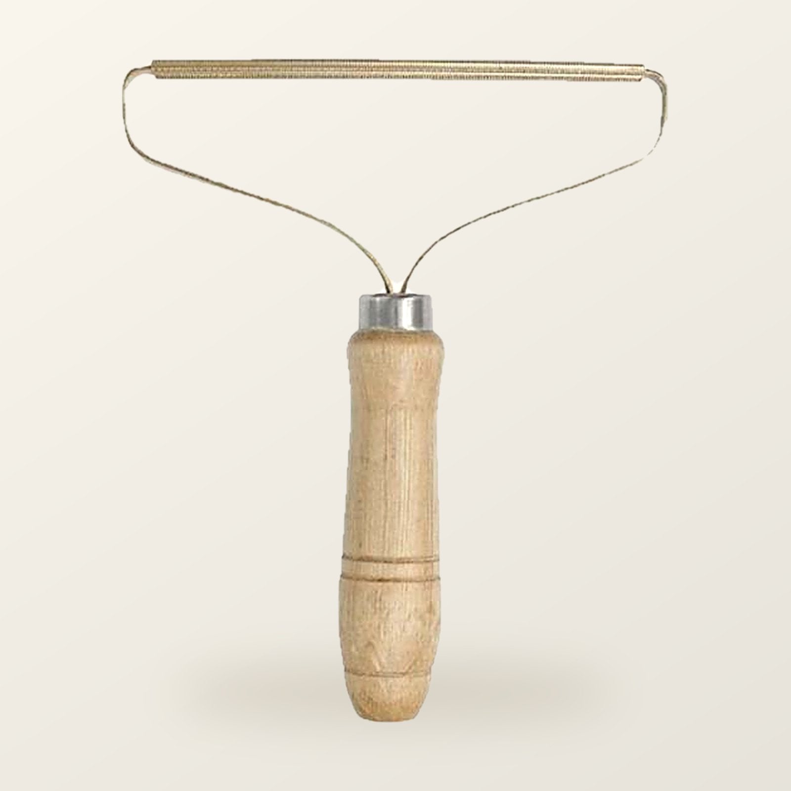 Fur lifter with a turned wood handle and a slim brass blade on a wire frame, on a warm cream background