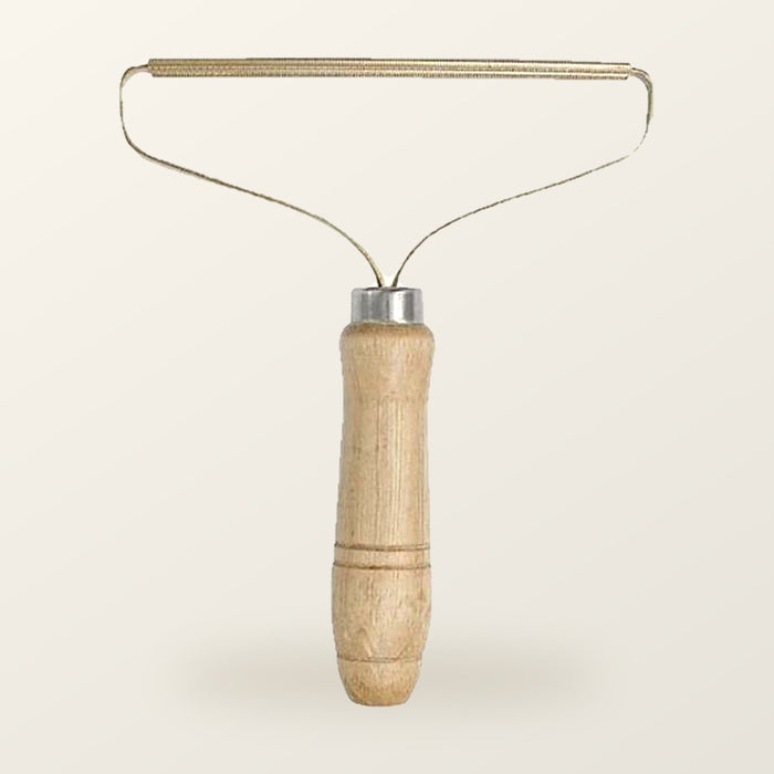 Fur lifter with a turned wood handle and a slim brass blade on a wire frame, on a warm cream background