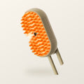 The shed brush: steam grooming brush with orange silicone bristles and a cream body, on a warm cream background