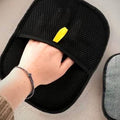 Black mesh hair-removal mitt worn on a hand, sweeping a pale sofa