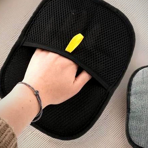 Black mesh hair-removal mitt worn on a hand, sweeping a pale sofa